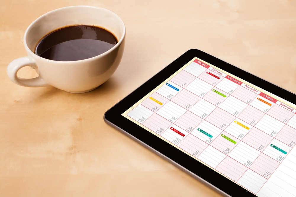 Workplace with tablet pc showing calendar and a cup of coffee on a wooden work table close-up Workplace with tablet pc showing calendar and a cup of coffee on a wooden work table close-up